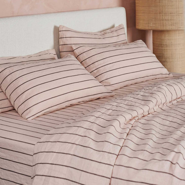 Bed with striped bedding and a lamp against a pink wall